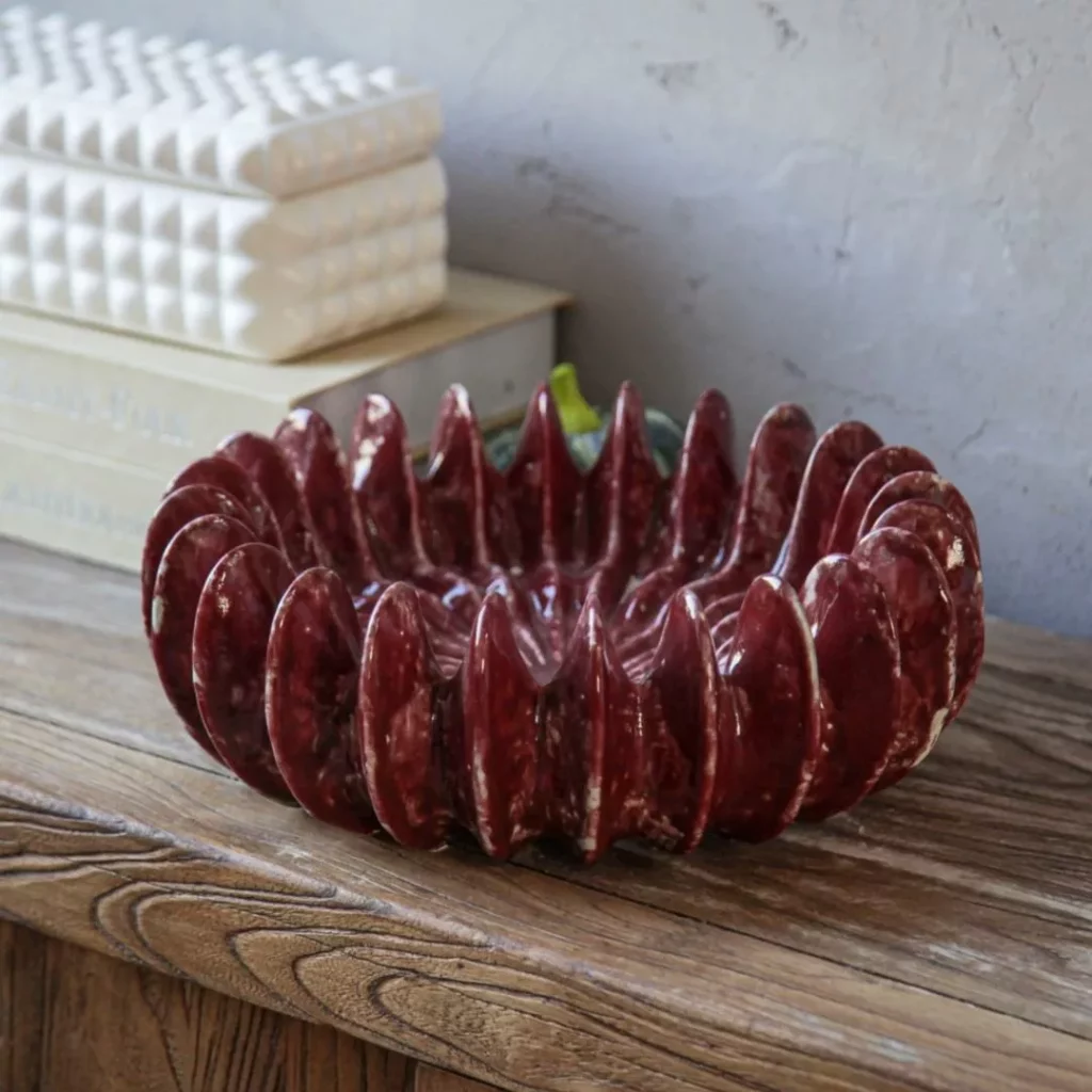 Artisanal marbled red-and-white ceramic vase with a textured, organic shape, holding a bouquet of dried pink roses, styled on a wooden book titled 