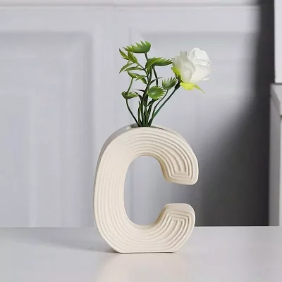 Vibrant A, B, C letter-shaped ceramic vases in yellow, orange, and cream, with the 'A' vase holding a bouquet of artificial white flowers, styled on a modern home desk.