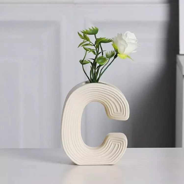 Vibrant A, B, C letter-shaped ceramic vases in yellow, orange, and cream, with the 'A' vase holding a bouquet of artificial white flowers, styled on a modern home desk.