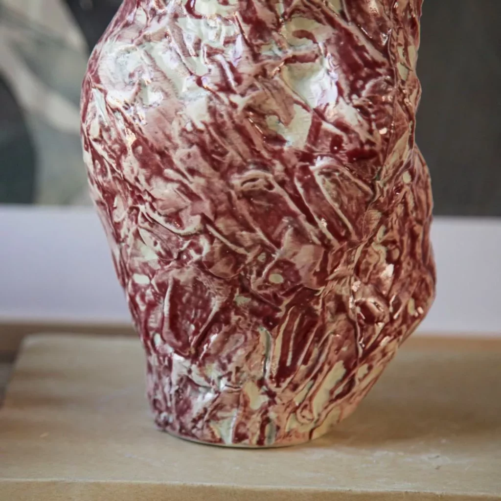 Artisanal marbled red-and-white ceramic vase with a textured, organic shape, holding a bouquet of dried pink roses, styled on a wooden book titled 
